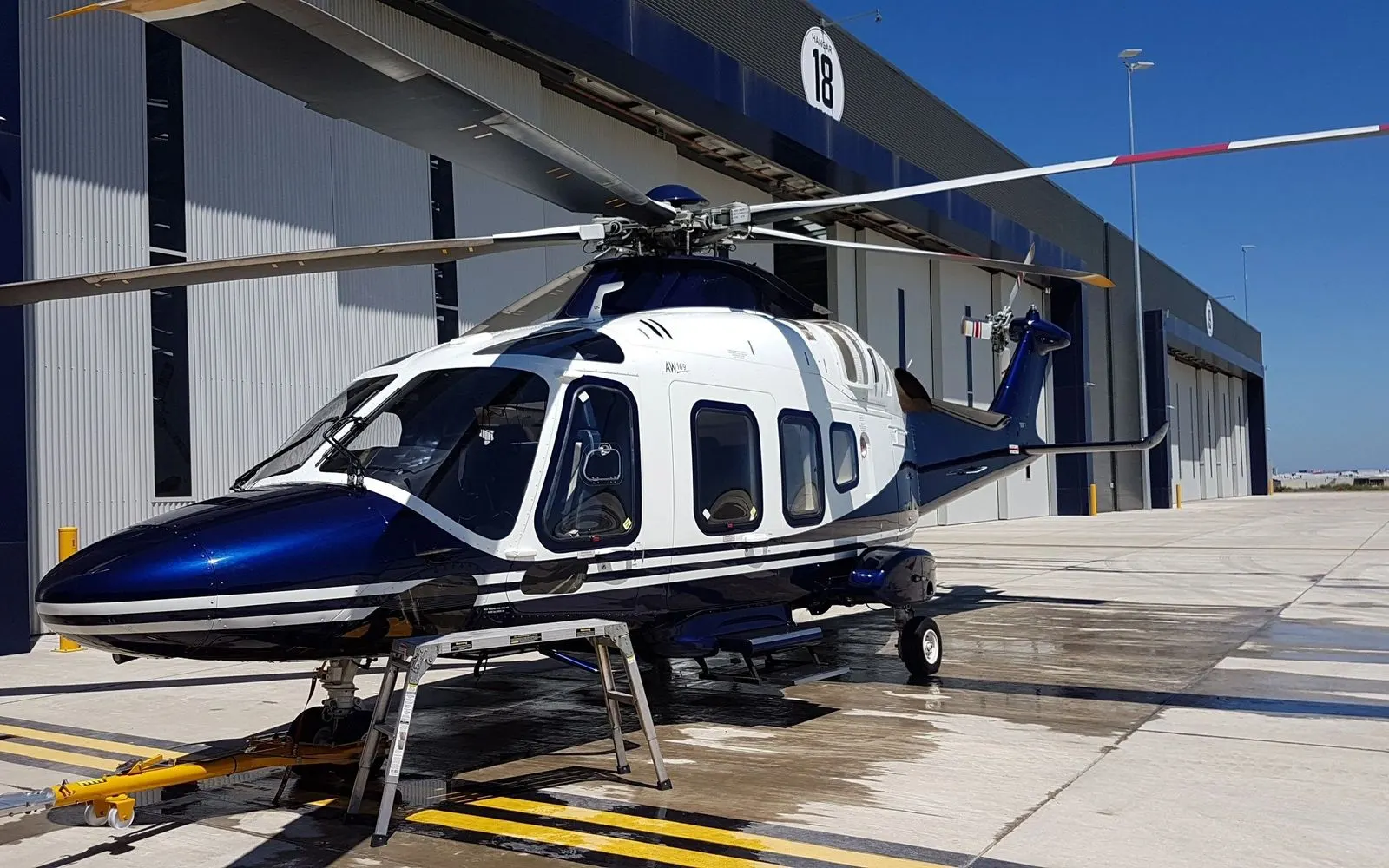 Blue and white helicopter beside a hangar on a freshly washed ramp