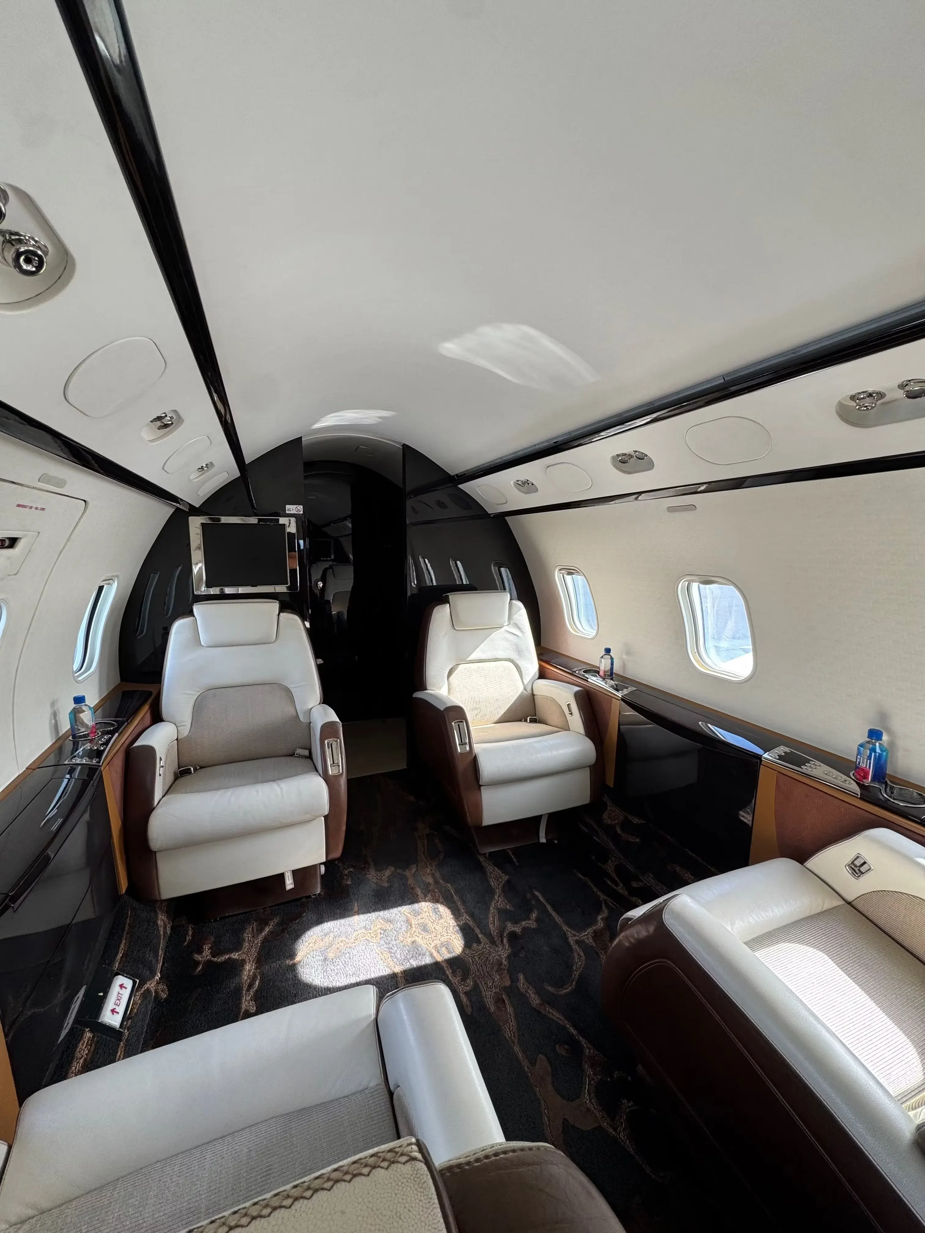 Large-cabin business jet interior with tan leather seating, dark veneer and stone table